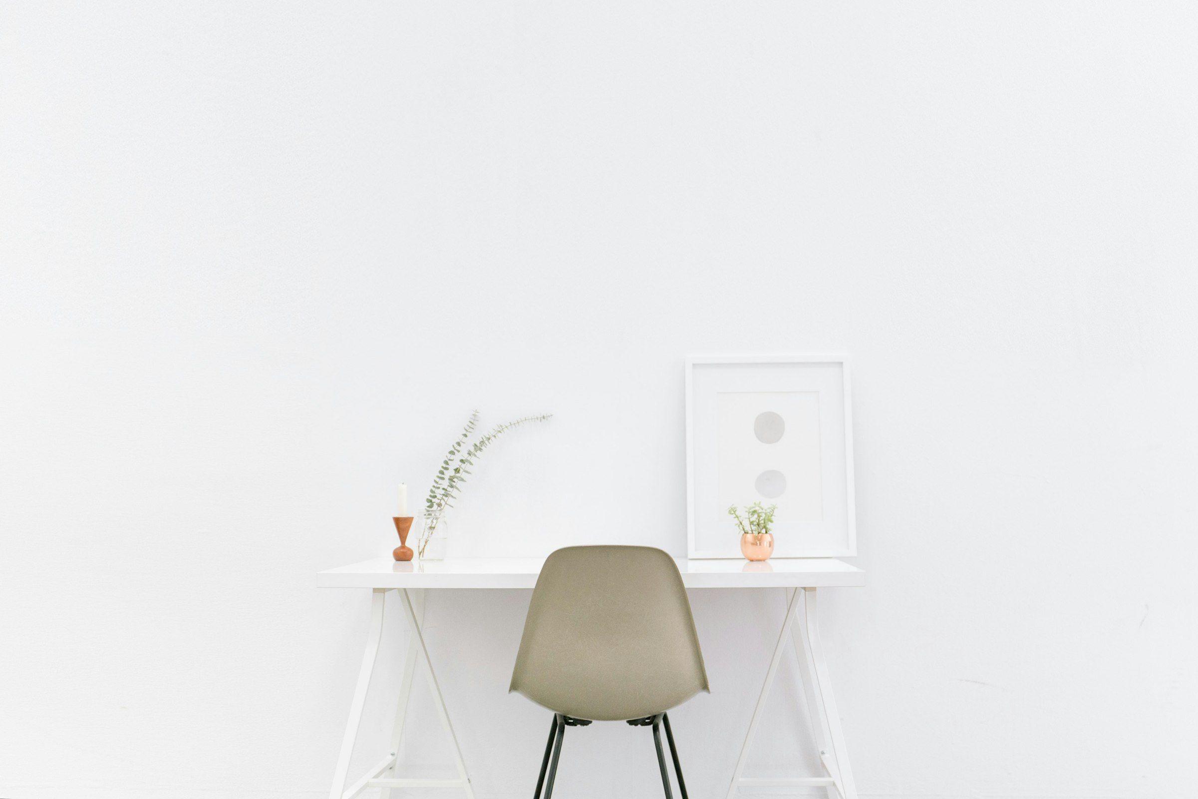 Minimal white desk with a single chair against a plain wall