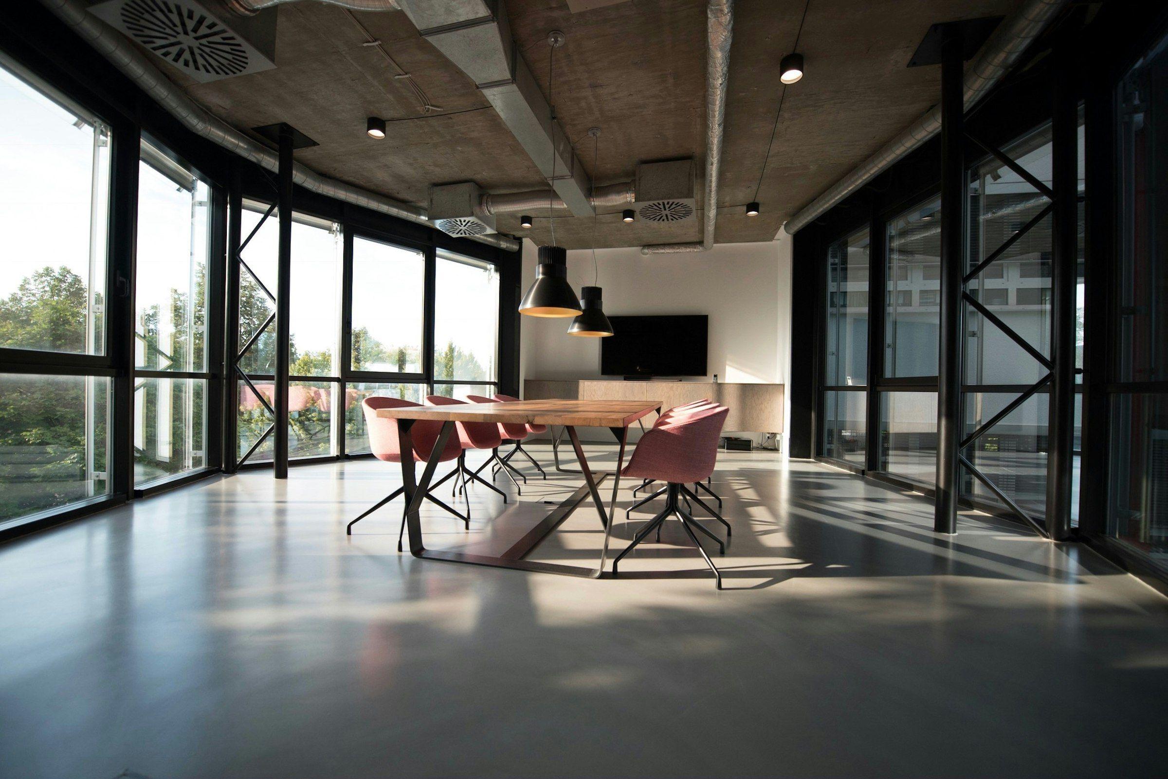 A long shared table under tall windows in an open studio floor fitted with Unit components